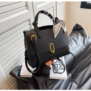 Detail of black woven leather handbag featuring a gold U-lock and silk scarf handle