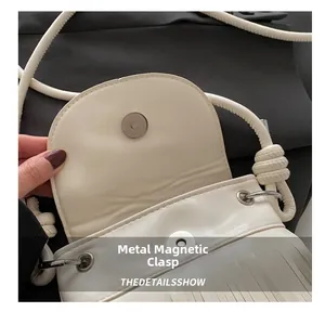Close-up of the magnetic hardware snap closure on a white tasseled crossbody bag