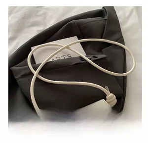 Detail of cream crossbody bag with silver bow buckle and knotted strap on gray blazer