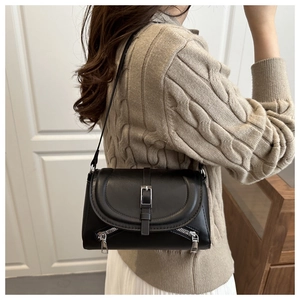 Detail of a black leather shoulder bag with decorative silver zippers and flap cover