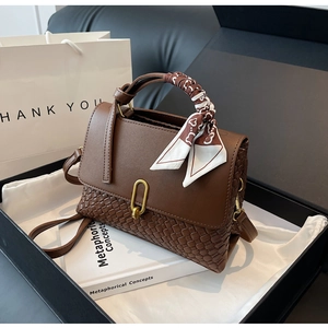 Detail view of brown leather handbag with woven texture and decorative silk scarf wrap