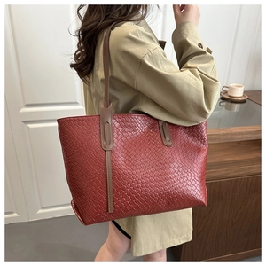 Dettaglio della borsa tote intrecciata rosso-marrone con tracolla indossata da modella