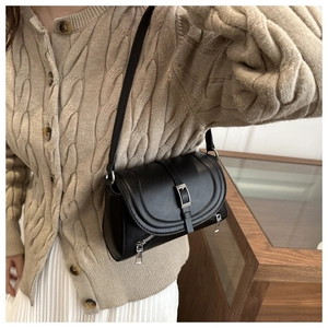 Close-up of black matte leather saddle bag featuring metal buckle and textured strap