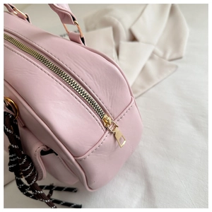 Detail shot of pale pink faux leather handbag with gold zipper and woven charm strap