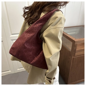 Detailed view of burgundy tote bag featuring leopard texture and wide shoulder strap