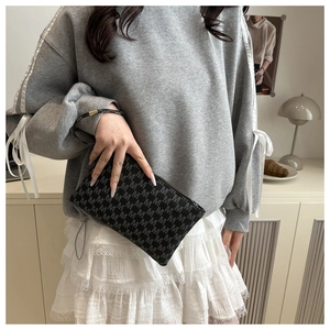 Detail of minimalist black envelope clutch bag featuring repeated M-letter print and wristlet