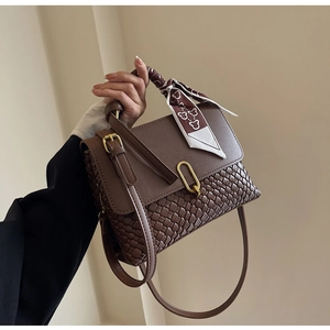 Detail of dark brown leather handbag with woven texture and gold oval metallic lock