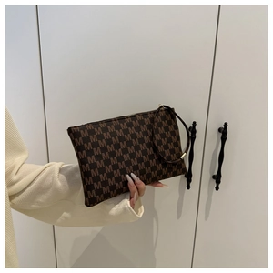 Close-up of brown clutch bag featuring M-letter print and zipper with hand strap