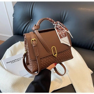 Brown woven crossbody bag with a decorative silk scarf, placed on a white tweed jacket