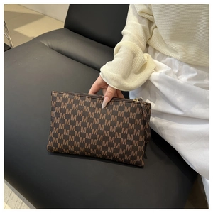 Detail of a brown clutch with M letter monogram pattern and high-quality metal zipper
