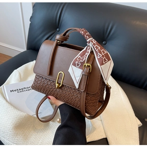 Detail of woven leather handbag with golden U-shaped clasp and decorative silk scarf