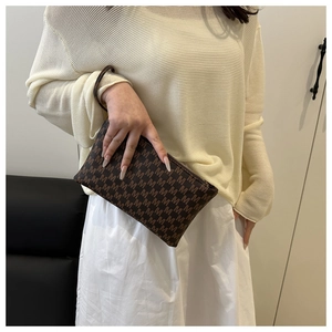 Close-up of brown letter jacquard envelope clutch bag with leather wristlet strap
