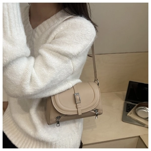 Detail of beige leather crossbody bag featuring metal buckle and decorative zippers
