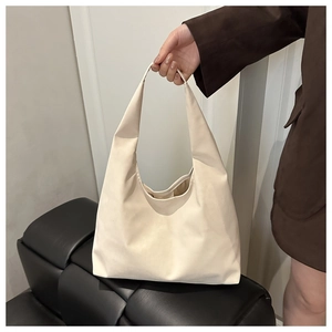 Close-up of a minimalist cream hobo bag held by a model wearing a brown blazer