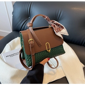 Detail view of woven dark green texture and brown leather flap with golden oval clasp