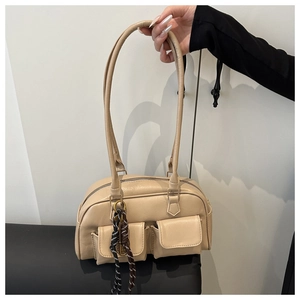 Detail of cream underarm bag featuring two front pockets and woven ring charm accessory