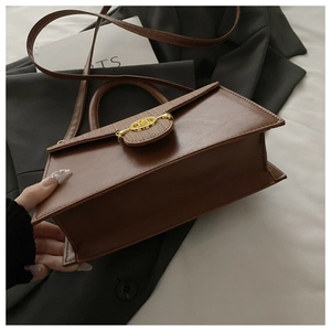 Nahaufnahme der braunen Leder-Handtasche mit goldener Schnalle auf Outfit-Hintergrund