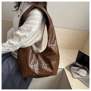 Detailed view of brown tote bag with silver metal star rivet design and wide shoulder strap