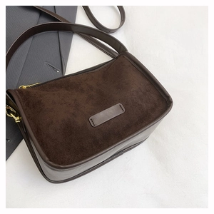 Detailed view of dark brown frosted suede shoulder bag paired with gray suit jacket