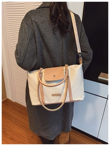 Detail of off-white tote bag with brown leather trim and metal fashion logo plate