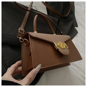 Detail einer braunen Umhängetasche mit Tweed-Patchwork und goldener runder Metallschnalle