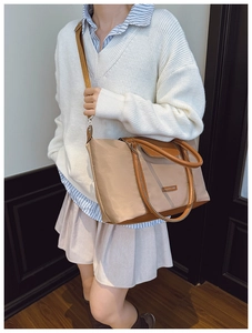 Close-up of a large beige nylon tote bag with brown leather handles and adjustable strap