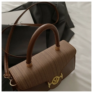 Detail einer braunen Ledertasche mit gewebter Klappe und goldener M-förmiger Schnalle