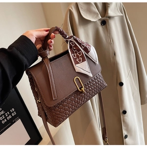 Detail of a brown leather handbag with woven texture, golden lock, and decorative silk scarf