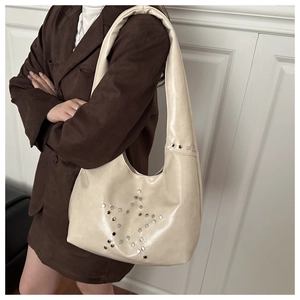 Detail of silver star-shaped rivets on cream leather shoulder bag worn by model