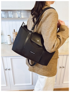 Close-up of black nylon tote bag with front pocket flap and metallic ring handle detail