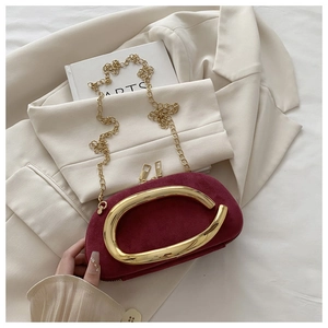Détail du sac de soirée en daim bordeaux avec poignée dorée en C sur une veste beige