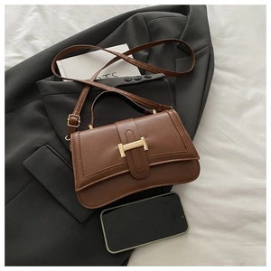 Detail of vintage dark brown faux leather handbag with golden lock on gray suit fabric
