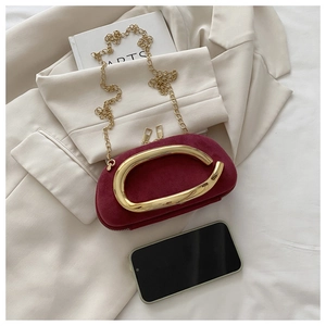 Detail of burgundy suede round clutch bag with gold C-handle on a beige blazer background
