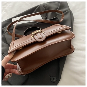 Detail of brown leather shoulder bag with gold buckle and adjustable strap