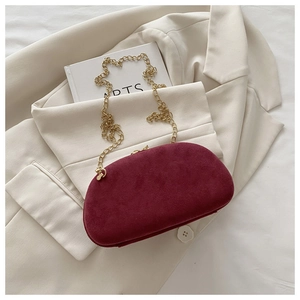 Detail of burgundy suede clamshell clutch with gold metal chain on beige suit