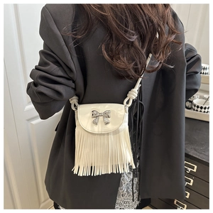 Detail view of a white crossbody bag with silver bow and flowing fringe tassels on model