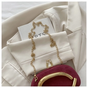 Détail pochette en velours bordeaux avec poignée ronde dorée et chaîne sur veste beige