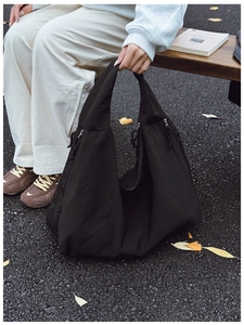 Detail of black nylon tote bag featuring functional side zipper and drawstring pocket design