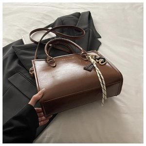 Détail d'un sac cabas en similicuir marron foncé avec breloque chocolat sur un lit