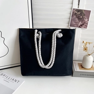 Close-up of black canvas tote bag featuring thick white cotton rope handles and metal eyelets