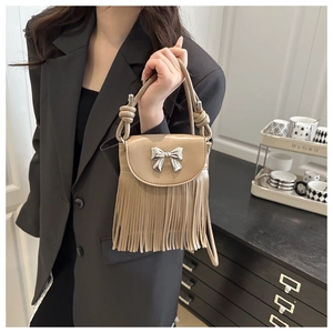 Close-up of khaki crossbody bag with fringe tassels, silver bow and knot handle detail
