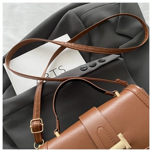 Detail of brown faux leather handbag with gold T-lock and textured finish on grey suit