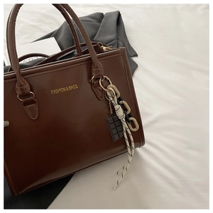 Détail du sac cabas marron foncé avec logo doré et breloques chocolat sur tissu blanc plissé