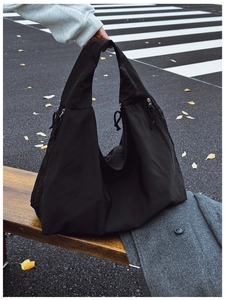 Detail of black canvas tote bag with side zippers on a wooden bench in autumn setting
