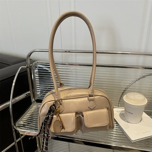 Retro beige shoulder bag with dual front flap pockets and tennis racket charm on a metal cart