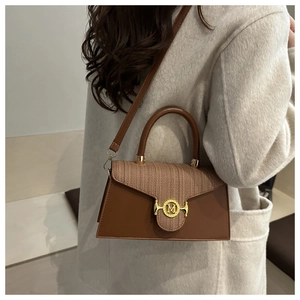 Detail of a brown patchwork handbag with tweed flap and golden M buckle on a beige coat