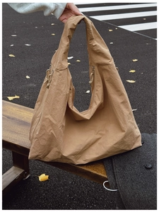 Detail view of camel nylon tote bag with side zipper and drawstring on a bench