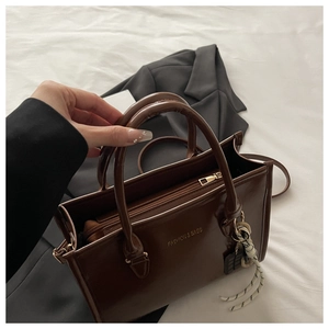 Détail du sac cabas en cuir marron foncé avec fermeture éclair dorée et pendentif