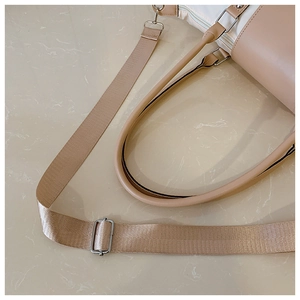 Detail of bicolor bag showing wide fabric shoulder strap with silver buckle and leather handle