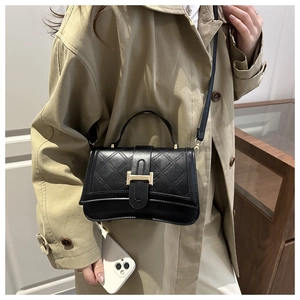 Detail of black quilted leather shoulder bag with gold H clasp on camel trench coat